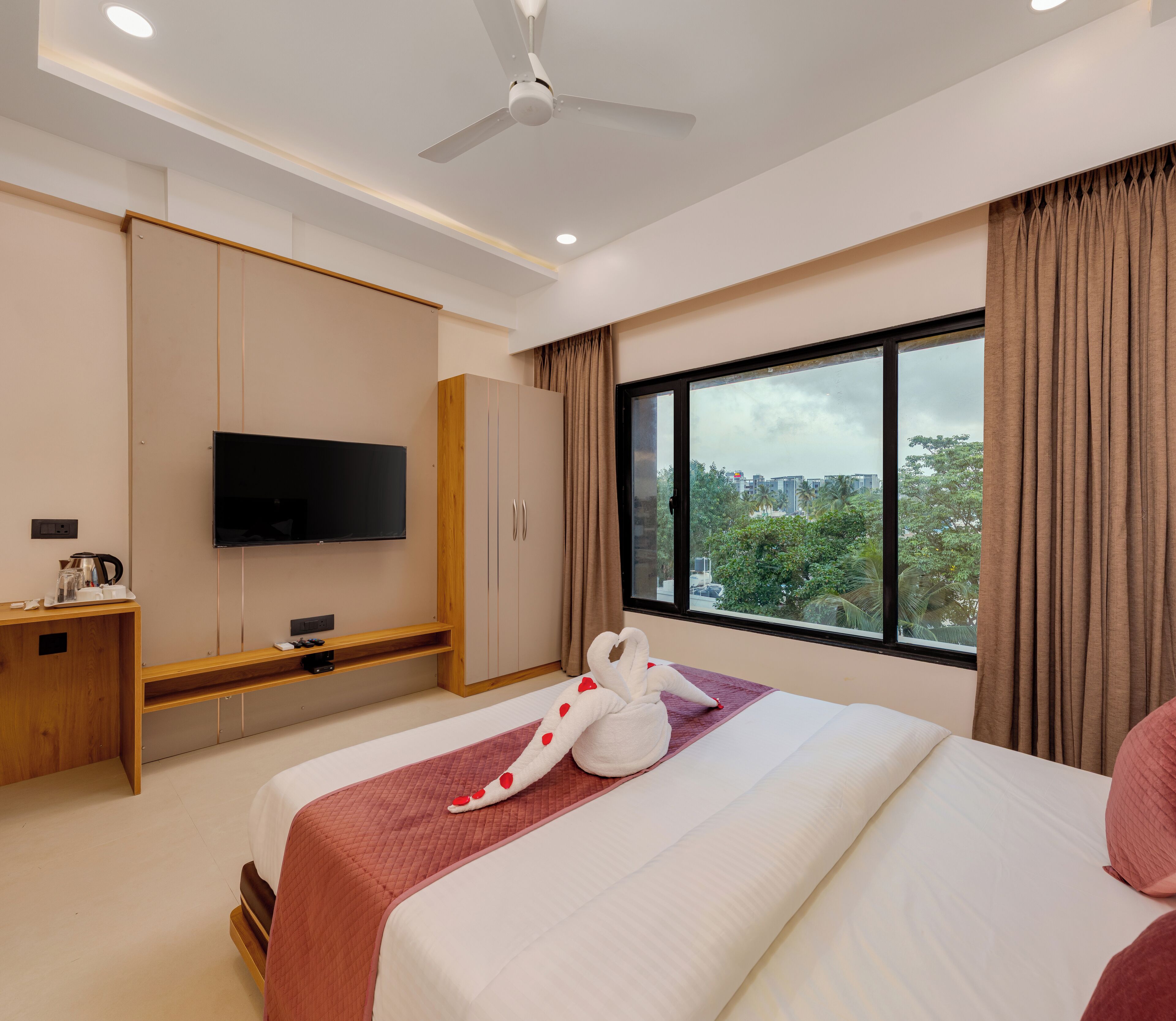 A hotel room with a bed, a TV, a desk, and a window with curtains.