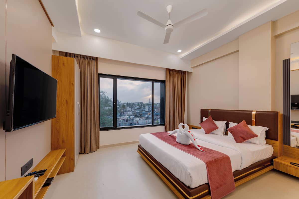 A modern hotel room with a large bed, a flat-screen TV, a wooden bench, and a city view.