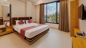 A modern hotel room with a large bed, a TV, a desk, and a window with a city view. - Hotel The Container (Kolhapur)