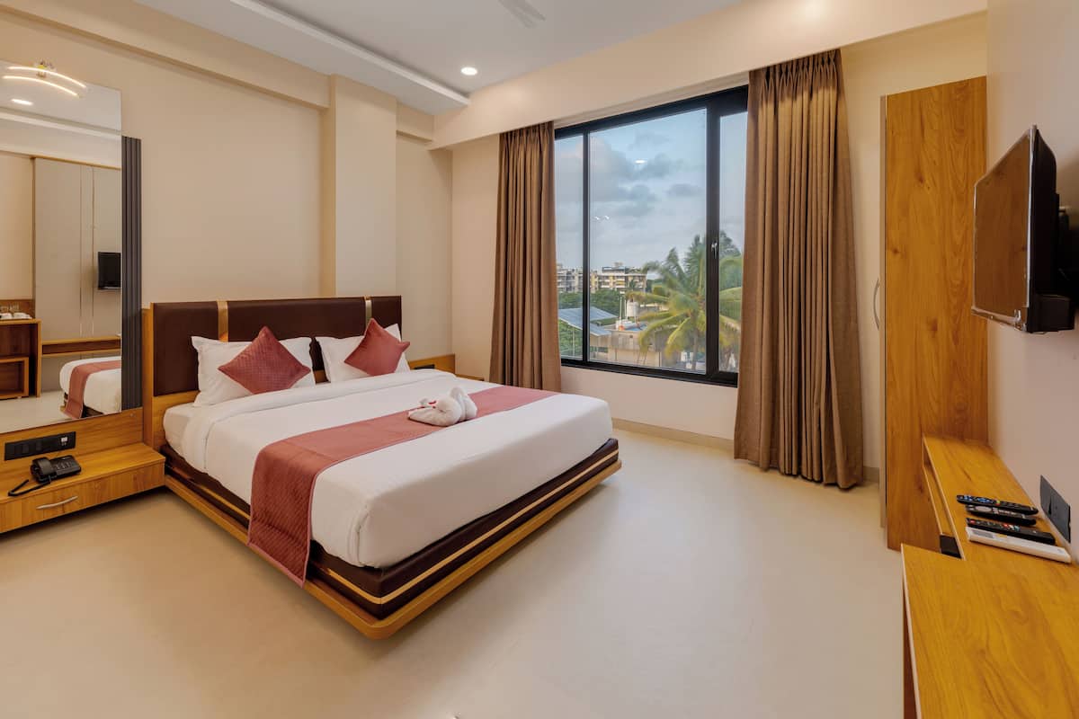 A modern hotel room with a large bed, a TV, a desk, and a window with a city view.