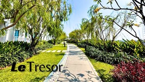 Un chemin bordé d’une végétation luxuriante et d’arbres, qui mène à un bâtiment à la façade blanche et aux fenêtres bleues.