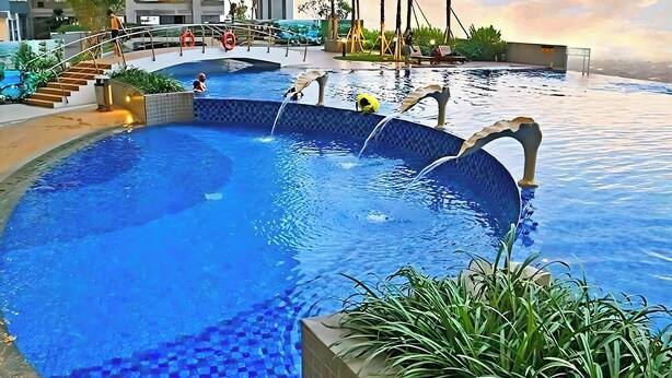 Une piscine agrémentée d’une cascade, entourée de palmiers et bordée d’un bâtiment moderne.