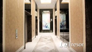 Un couloir d’hôtel moderne avec un sol à motifs géométriques, des murs recouverts de miroirs et un luminaire central.
