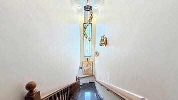 Una escalera con barandilla de madera, suelo de mármol y una lámpara fijada a la pared.