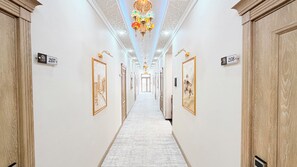 A hotel hallway with a white carpet, numbered doors, and framed artwork on the walls. - Saroy Khiva (Khiva)