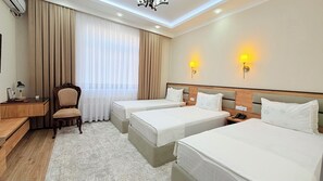 A hotel room with two beds, a desk with a chair, a lamp, and a window with curtains. - Saroy Khiva (Khiva)