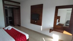 A modern hotel room with a large bed, a TV mounted on the wall, and a mirror above the bed. - JB Residency (Tiruchirappalli)