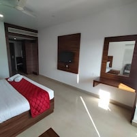 A modern hotel room with a large bed, a TV mounted on the wall, and a mirror above the bed.