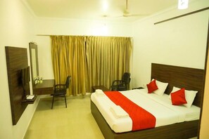A hotel room with a bed, a desk, a chair, a TV, and a window with curtains. - JB Residency (Tiruchirappalli)