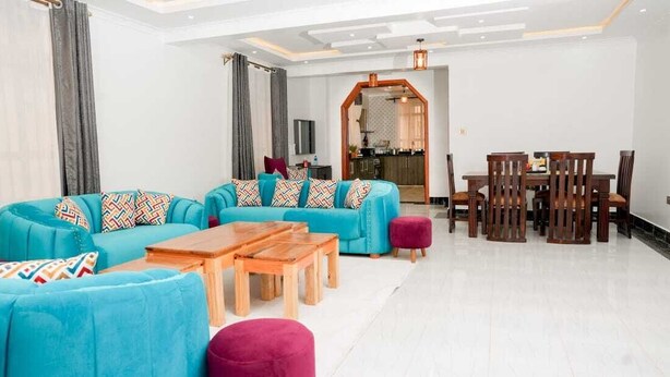 A modern living room with a sectional sofa, wooden coffee table, and dining area with wooden chairs. - Lux Suites Advent Homes Naivasha (Naivasha)