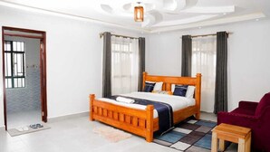A bedroom with a wooden bed, a red chair, and a small wooden table. - Lux Suites Advent Homes Naivasha (Naivasha)
