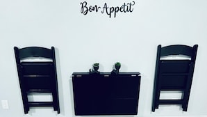 Una habitació amb dues cadires negres a cada costat d'una consola negra, una petita planta en test i un cartell al mur que diu "Bon Appetit".