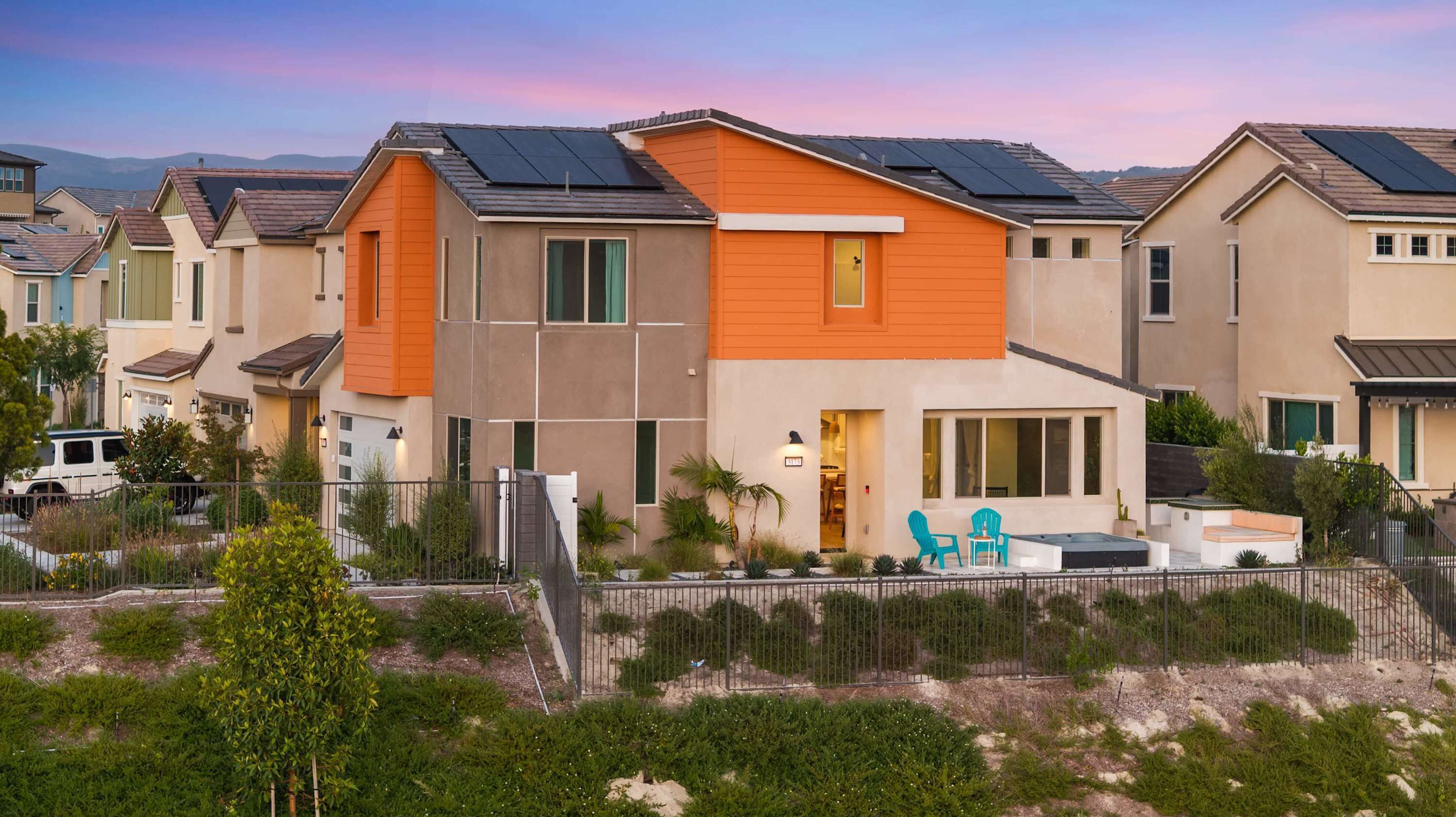 A residential area with modern houses featuring solar panels, a fenced yard with greenery, and outdoor seating.