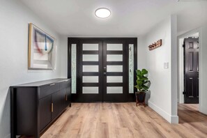 Un pasillo con una puerta negra, un radiador, una planta en maceta y un cuadro en la pared.