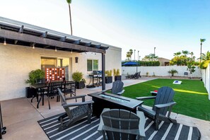 Un patio al aire libre con una parrilla, zona de estar y un césped bien cuidado.