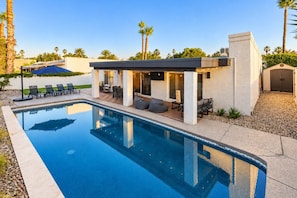 A modern poolside area with a clear blue pool, outdoor seating, and palm trees.