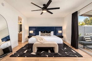A modern bedroom with a large bed, a ceiling fan, and a view of the outdoors.