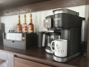 Una cafetera amb una tassa que diu “TRAVLI” sobre una superfície de fusta.