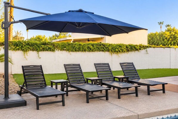 A poolside area with four lounge chairs and a large umbrella.