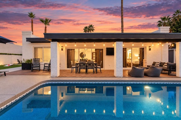 A modern house with a swimming pool, outdoor seating, and a sunset view.