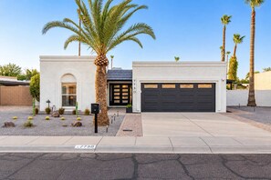 A modern two-story house with a garage, a driveway, and a well-maintained garden with palm trees and cacti.