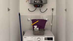 Pieni ja käytännöllinen pyykinhuoltotila, jossa on pyykinpesukone, lämminvesivaraaja ja moppi.