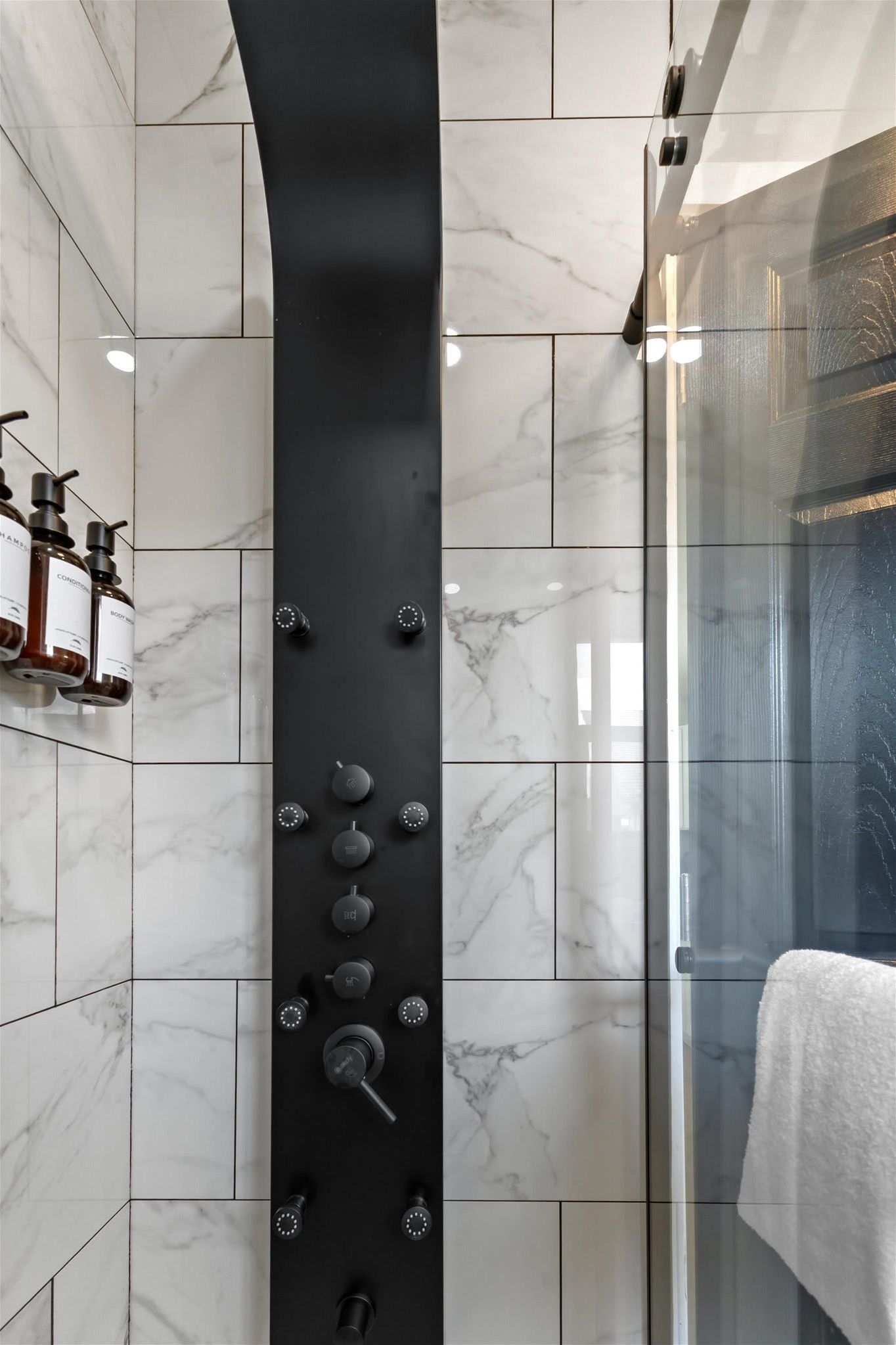 Une salle de bain moderne avec un panneau de douche noir, des carreaux de marbre et une paroi de douche en verre.