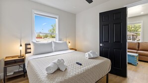 Ein ordentlich eingerichtetes Hotelzimmer mit einem großen Bett, einem Nachttisch mit Lampe, einem Fenster mit Blick und einer Tür zu einem weiteren Raum.