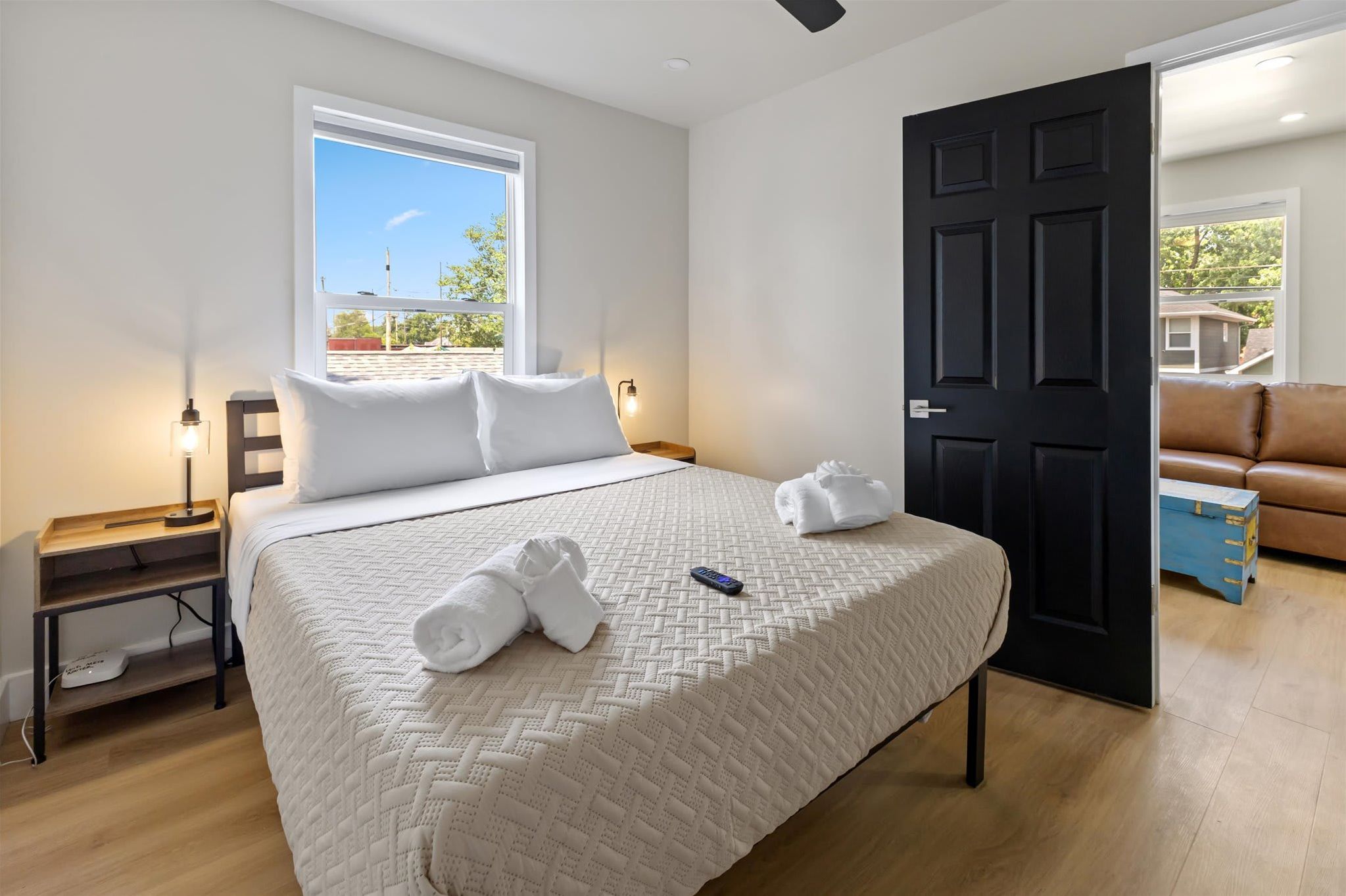Une chambre d’hôtel bien aménagée, avec un grand lit, une table de chevet avec une lampe, une fenêtre donnant sur un beau paysage et une porte menant à une autre pièce.