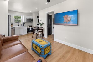 A modern living room with a brown leather sofa, a wooden coffee table, and a flat-screen TV mounted on the wall. - Modern Carriage House Indy (Indianapolis)