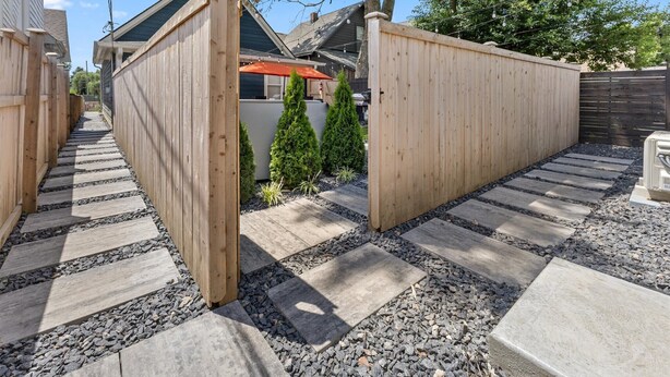 Ein Holzzaun mit einem Tor, ein Steinweg und ein kleiner Gartenbereich mit einem roten Sonnenschirm.