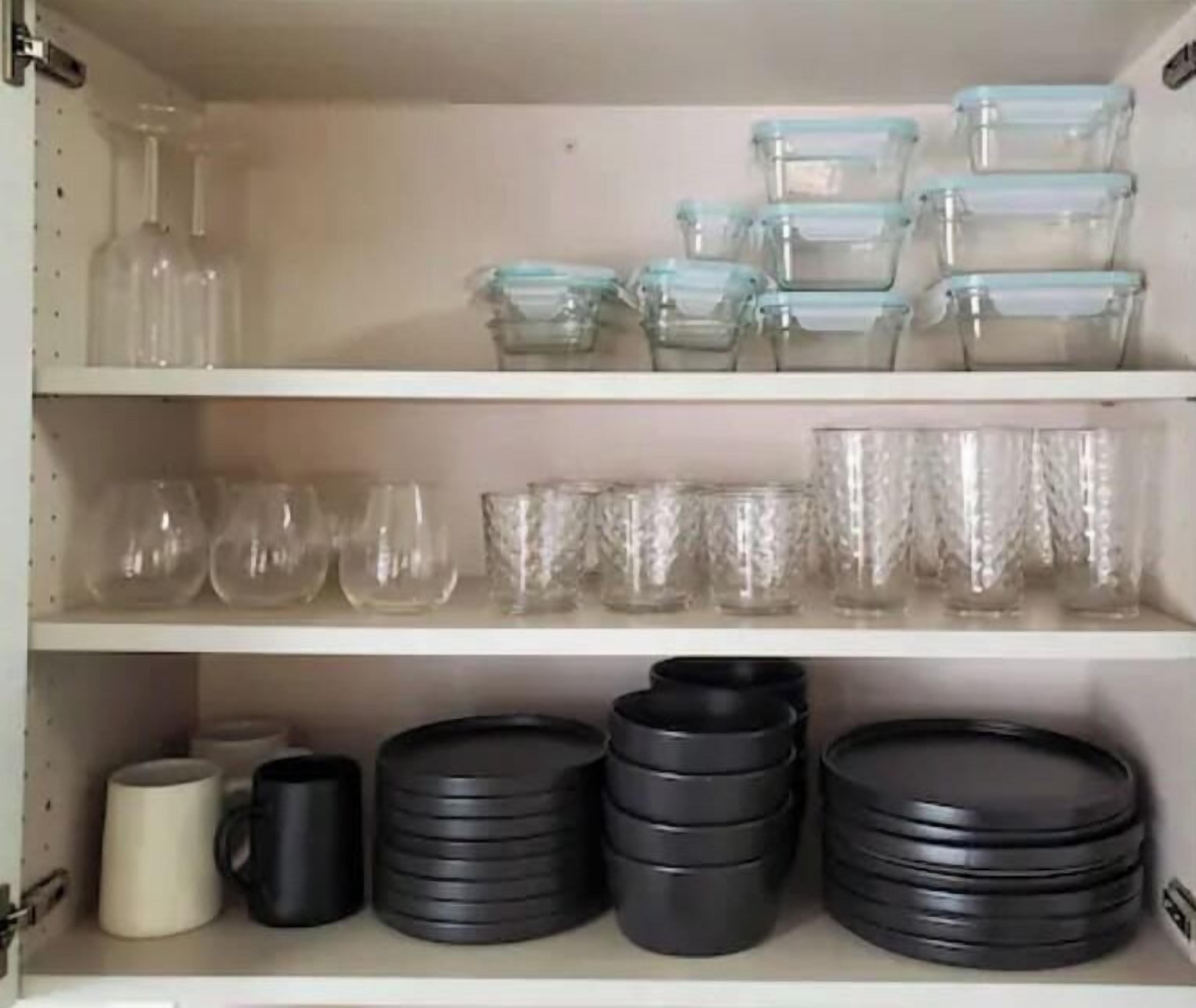 Uno scaffale in cucina con articoli in vetro, tra cui bottiglie di vino, bicchieri e tumbler.