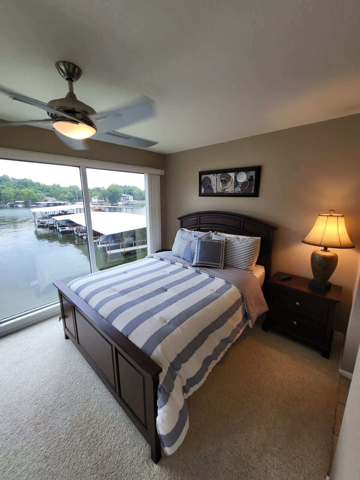 A bedroom with a large bed, a nightstand, a lamp, and a ceiling fan.