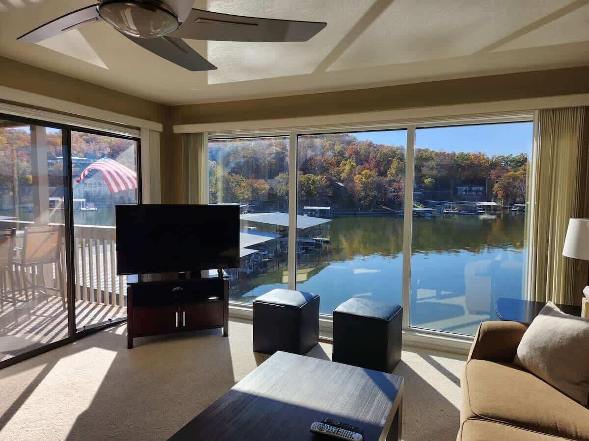 Un salon spacieux doté d’un grand téléviseur à écran plat, de sièges confortables et offrant une vue sur un lac où naviguent des bateaux.