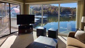 Un salon spacieux doté d’un grand téléviseur à écran plat, de sièges confortables et offrant une vue sur un lac où naviguent des bateaux.