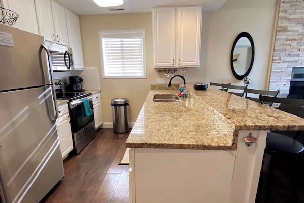 A kitchen with white cabinets, a granite countertop, stainless steel appliances, and a window with blinds.