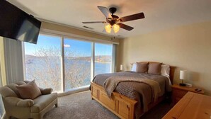 Une chambre dotée d’un grand lit, d’un ventilateur de plafond, d’une télévision et offrant une vue sur un lac grâce à de grandes fenêtres.