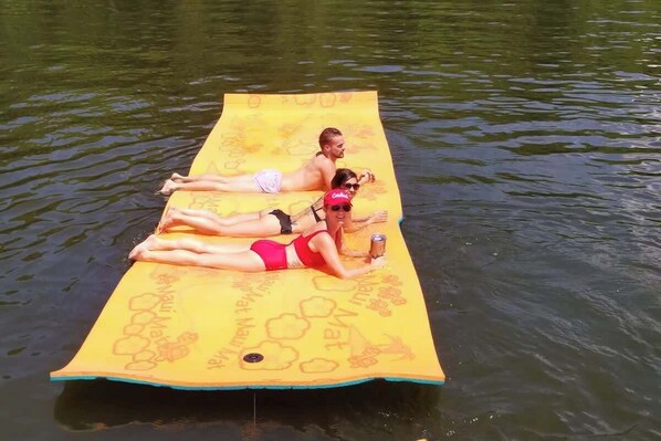 Dos personas reclinadas sobre una alfombra amarilla flotante en el agua.