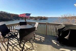A balcony with a table and chairs, an American flag, and a view of a river with boats.