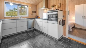 Una cocina moderna con armarios blancos, horno empotrado y ventana con vistas a zonas verdes.