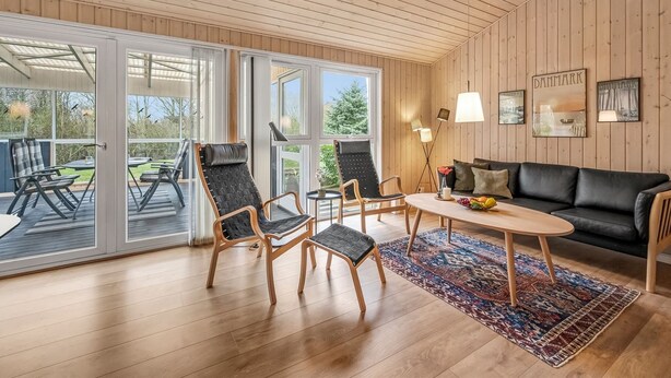 Un interior moderno con techo de madera, sofá de cuero negro, una mesa de centro y un área de comedor con sillas y alfombra.