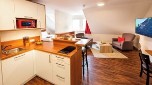 A compact kitchen with a microwave, sink, and wooden countertop. There is a dining area with a table and chairs, and a sofa with a red pillow.