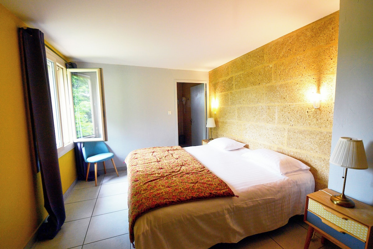 Una habitación de hotel con cama, una silla, una lámpara y una ventana con cortinas.