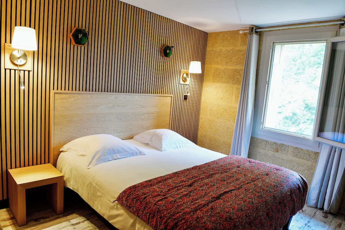 Una cama bien hecha con un edredón estampado, una mesita de noche y dos lámparas fijadas a la pared.