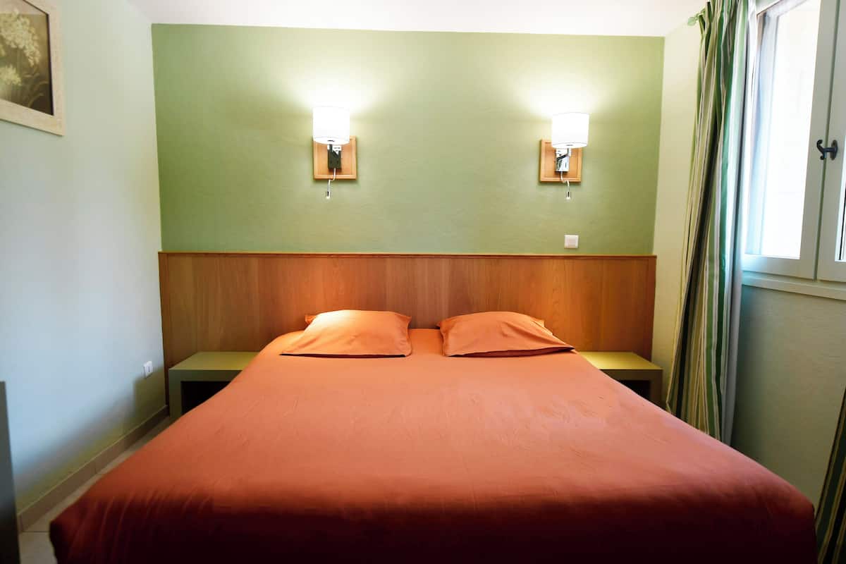 Una cama doble con colcha naranja, dos mesitas de noche y dos lámparas de pared.