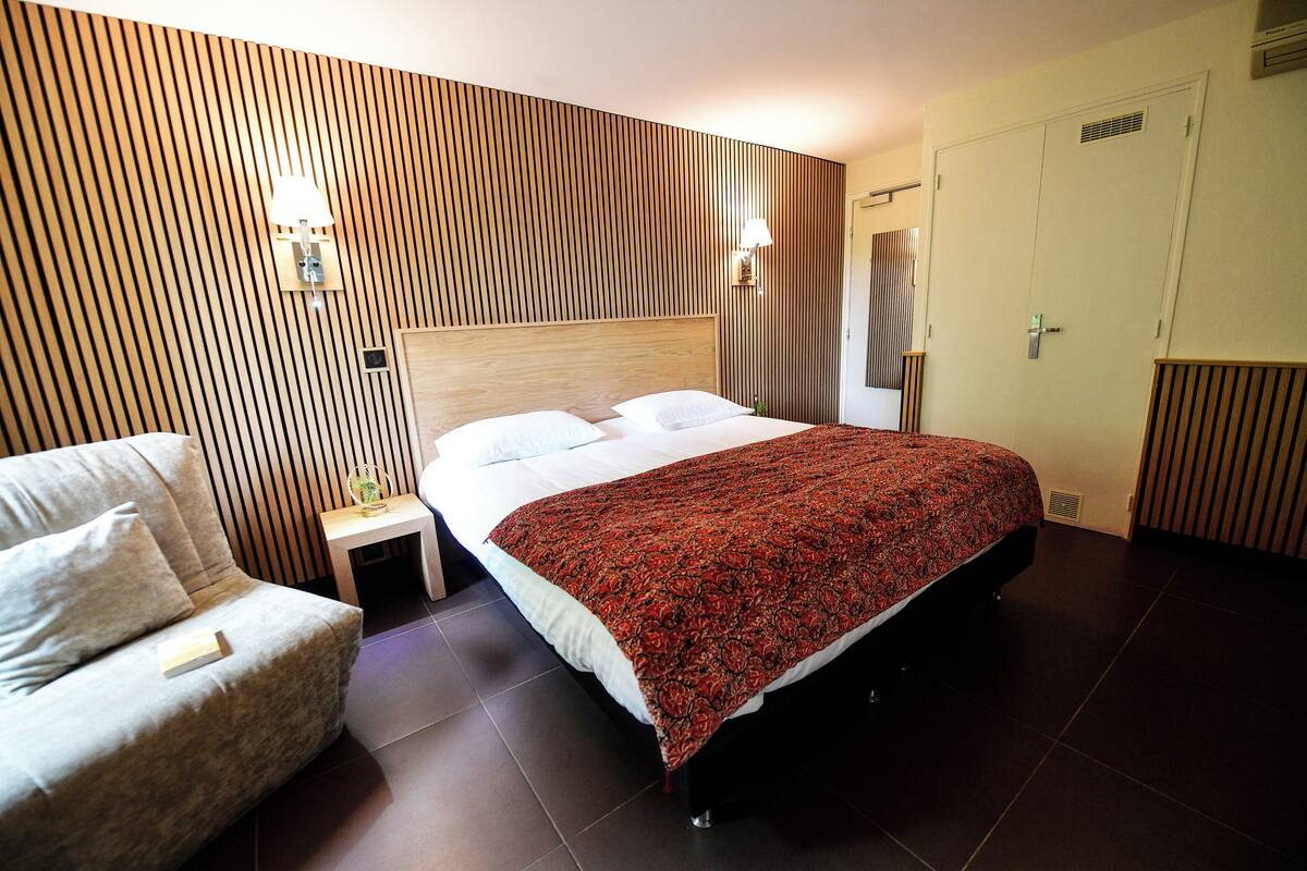 Una habitación de hotel con una cama, una mesita de noche, una silla y un panel de pared con listones de madera.