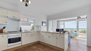 A modern kitchen with white cabinets, a built-in oven, and a view of the beach through large windows. - Beachfront Bungalow: Direct Access & Sea-View Terrace (Pevensey Bay)