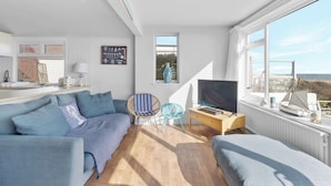 A modern living room with a sofa, a TV, and a view of the sea. - Beachfront Bungalow: Direct Access & Sea-View Terrace (Pevensey Bay)