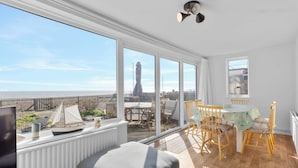 A room with a large window overlooking a beach, a dining area with wooden chairs, and a small table. - Beachfront Bungalow: Direct Access & Sea-View Terrace (Pevensey Bay)