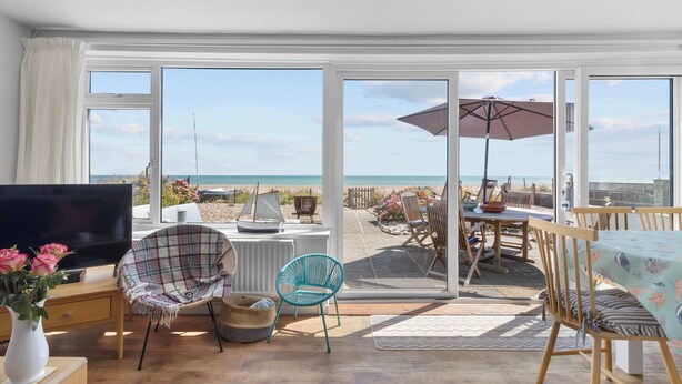 A spacious living room with a large TV, comfortable seating, and a view of the beach through large sliding doors. - Beachfront Bungalow: Direct Access & Sea-View Terrace (Pevensey Bay)